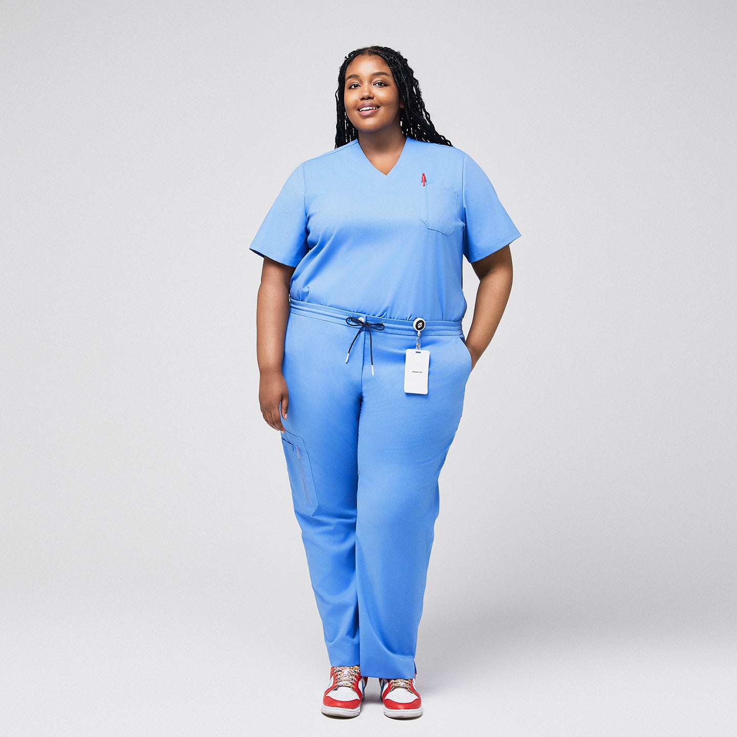 Plus-size model in light blue 3-pocket scrub top with matching pants, badge holder, and red sneakers, ideal for healthcare professionals,Ceil Blue