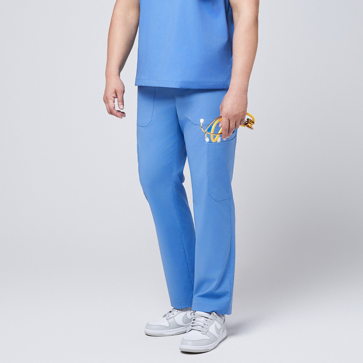 Side view of a person wearing ceil blue straight scrub pants featuring utility pockets, styled with white sneakers and holding a yellow stethoscope,Ceil Blue