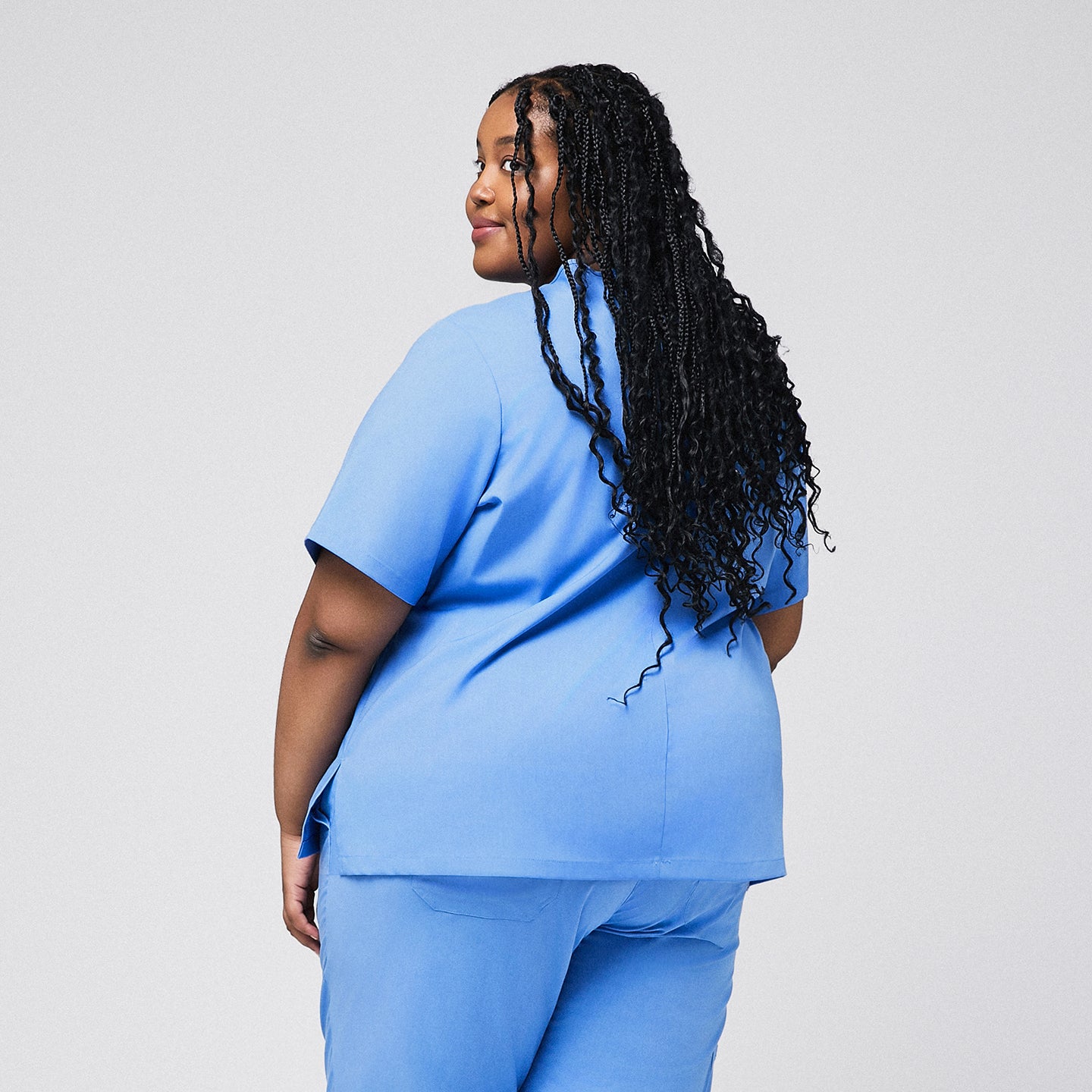 Back view of a plus-size healthcare professional in a ceil blue scrub set, looking over her shoulder with long braided hair flowing down her back,Ceil Blue