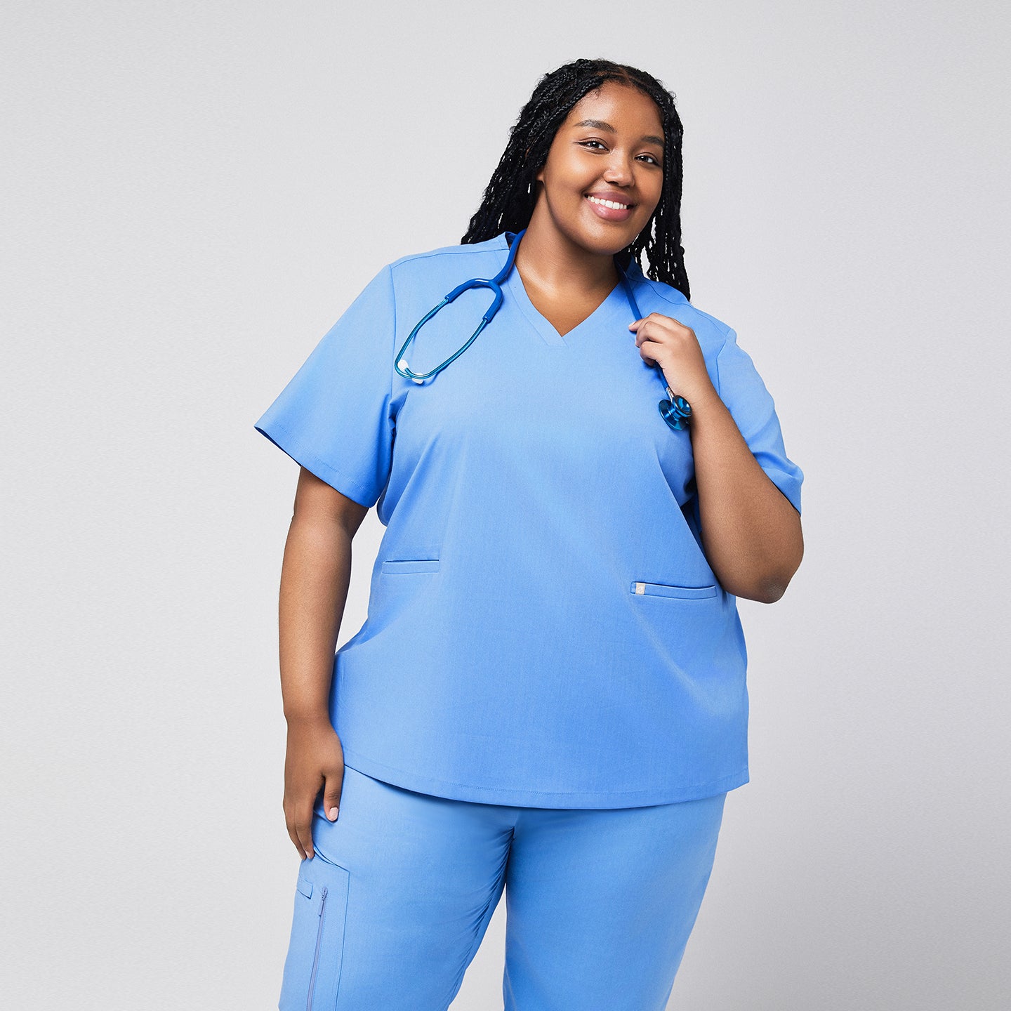 Plus-size healthcare professional wearing a ceil blue scrub set, holding a stethoscope over the shoulder, smiling with a front view,Ceil Blue