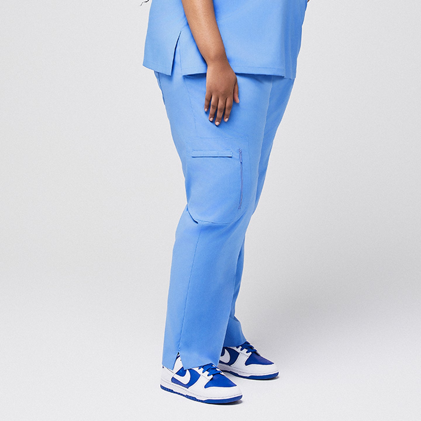 Blue scrub pants with zipper pocket and split hem, side view paired with blue sneakers,Ceil Blue