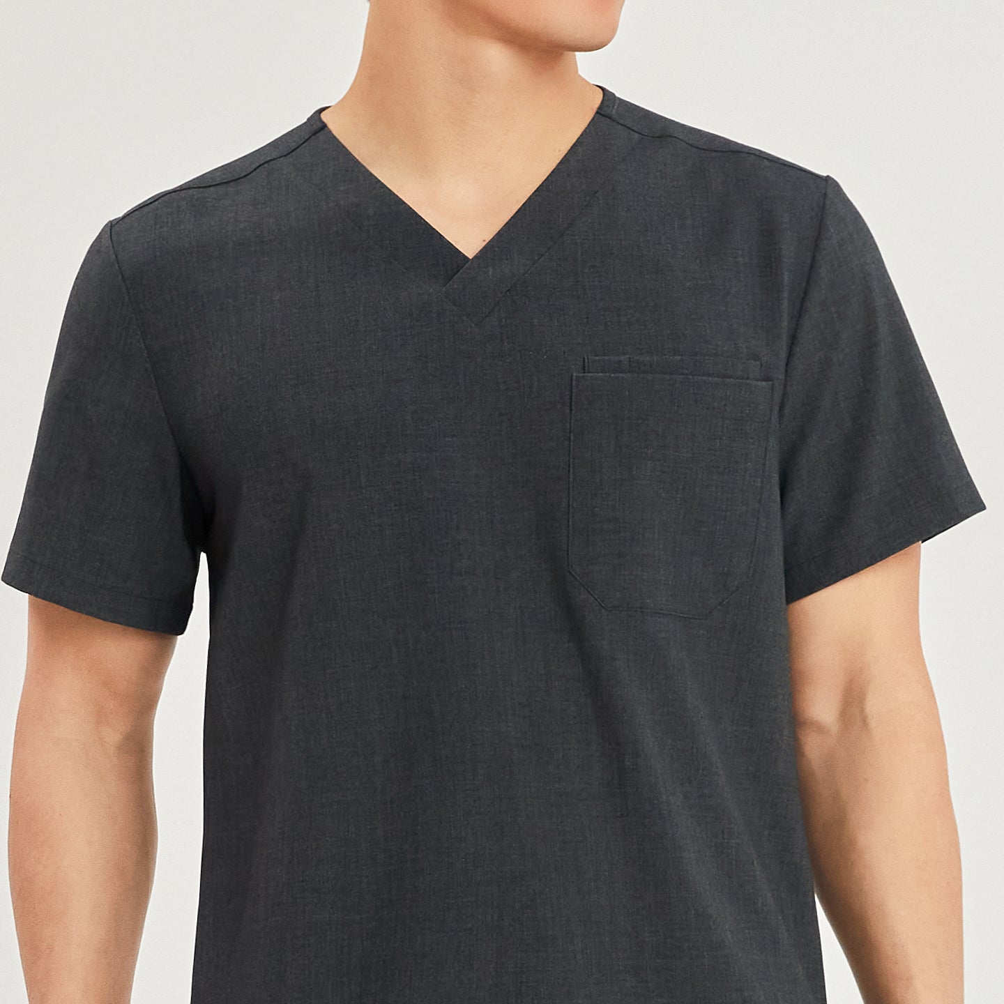 Close-up view of a male model wearing a charcoal gray scrub top with a V-neck and a single chest pocket. The focus is on the upper body and the pocket detail, Charcoal Gray