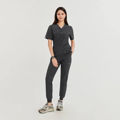 Female model wearing a charcoal gray 3-pocket scrub top with matching jogger-style pants and sneakers, offering a sleek and comfortable uniform for medical professionals,Charcoal Gray