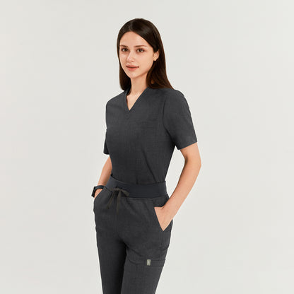 Female model wearing a charcoal gray 3-pocket scrub top and matching pants, hands in pockets, offering a sleek and functional uniform for healthcare professionals,Charcoal Gray