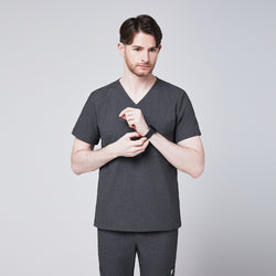 Image of Male healthcare professional wearing charcoal gray V-neck scrub top and pants, adjusting his smartwatch, standing against a plain background,Charcoal-Gray