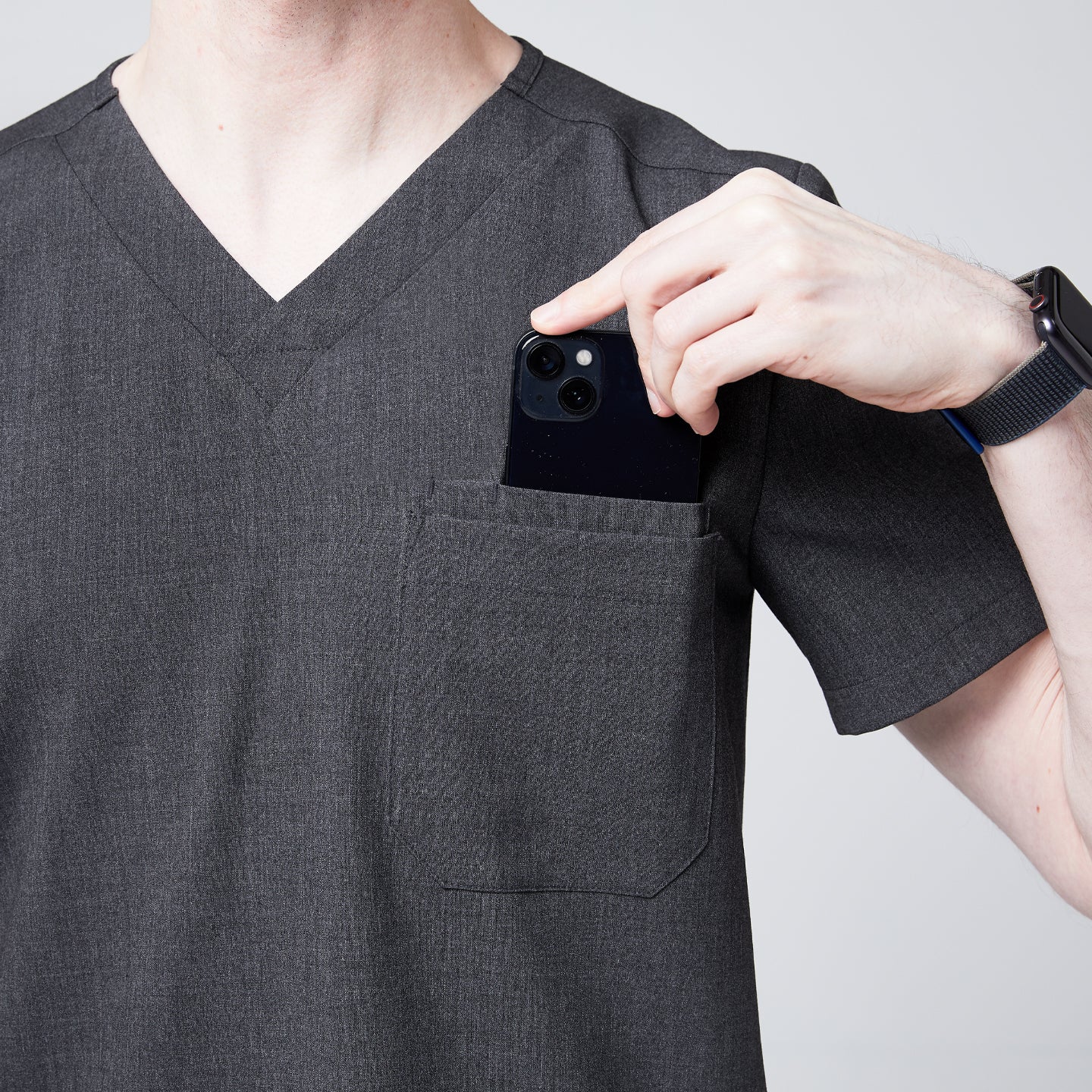 Male healthcare professional placing a smartphone into the chest pocket of a charcoal gray V-neck scrub top,Charcoal-Gray