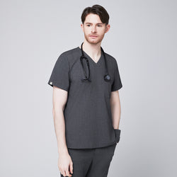 Image of Male healthcare professional in charcoal gray V-neck scrub top and pants, with black stethoscope around neck and hand in pocket, looking to the side,Charcoal-Gray