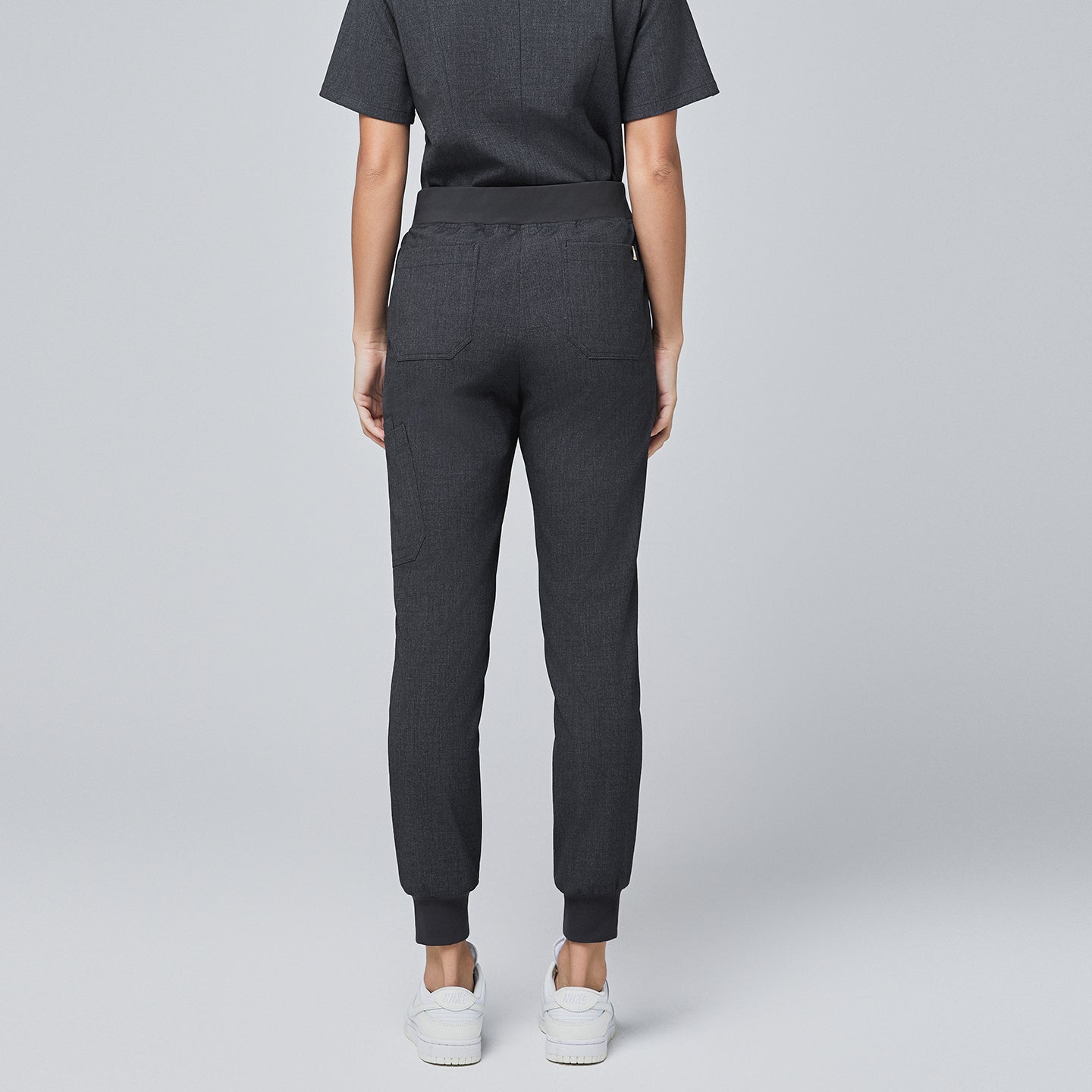 Back view of charcoal gray jogger scrub pants with rear pockets, elastic waistband, and cuffed ankles, paired with white sneakers,Charcoal Gray