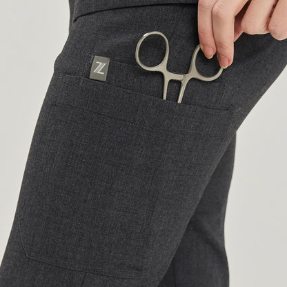  Close-up detail of charcoal gray jogger scrub pants showcasing a side pocket with medical scissors and a logo tag,Charcoal Gray