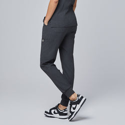 Image of Side view of charcoal gray jogger scrub pants featuring a side pocket, elastic waistband with a drawstring, and cuffed ankles, paired with white sneakers,Charcoal Gray