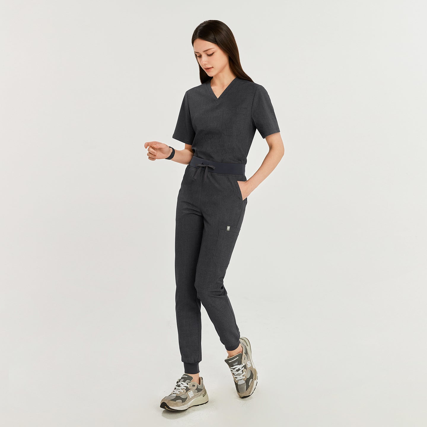 Woman wearing charcoal gray jogger scrub pants with a waistband tie, paired with gray sneakers,Charcoal Gray