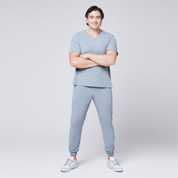 Image of Full-body view of a man in a cool gray scrub set with jogger pants, arms crossed, and wearing white sneakers,Cool Gray