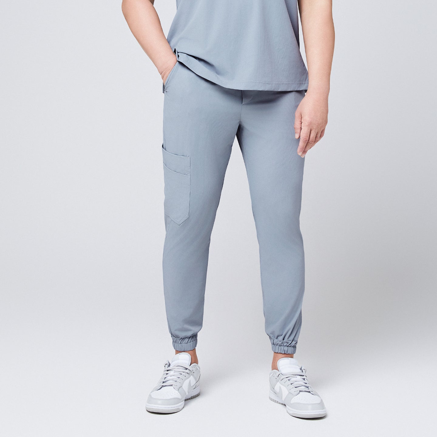 Front view of cool gray jogger scrub pants with a cargo pocket and elastic cuffs, paired with gray Nike sneakers,Cool Gray