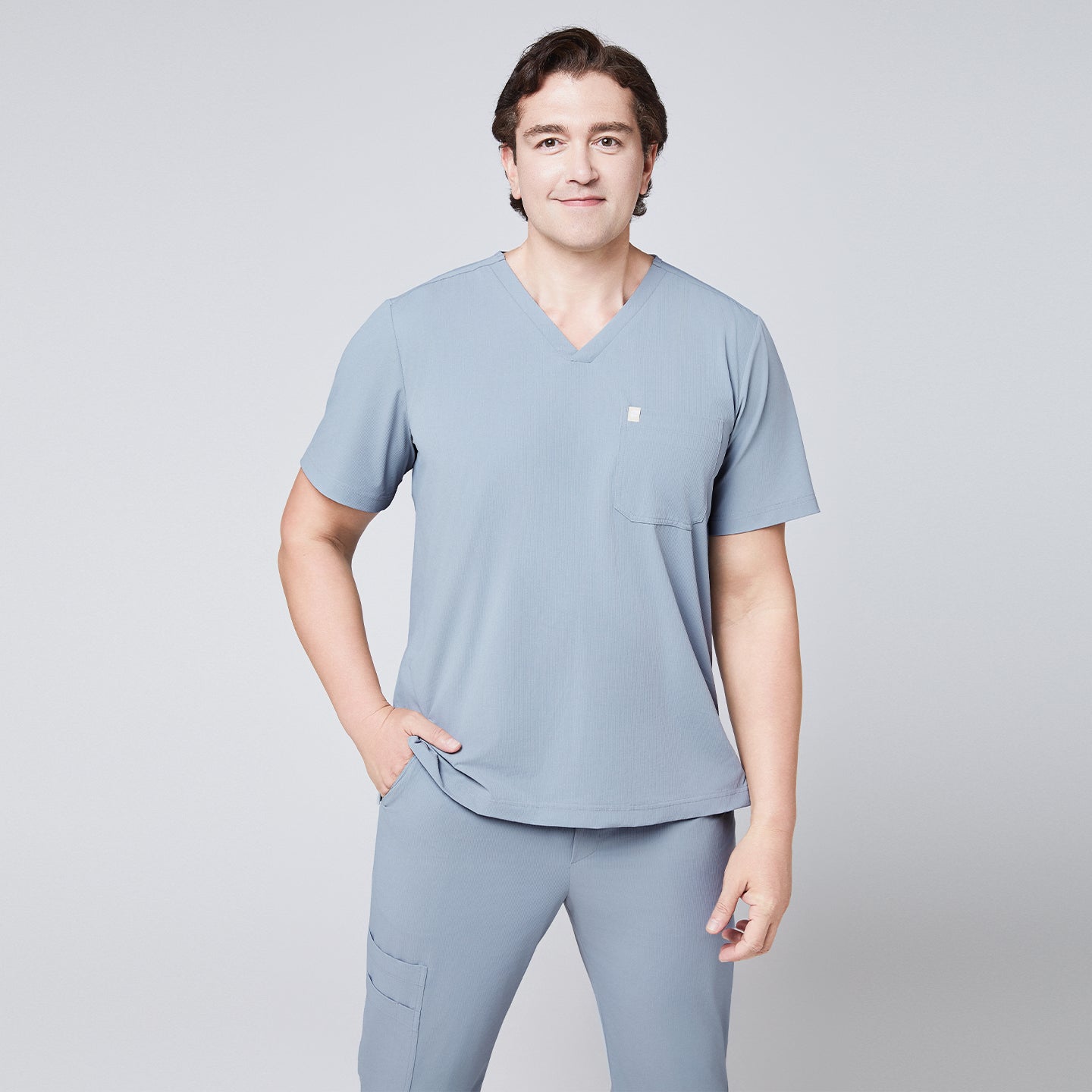 Model wearing a cool gray V-neck scrub top with a chest pocket and matching jogger scrub pants, styled casually,Cool Gray