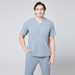 Image of Model wearing a cool gray V-neck scrub top with a chest pocket and matching jogger scrub pants, styled casually,Cool Gray