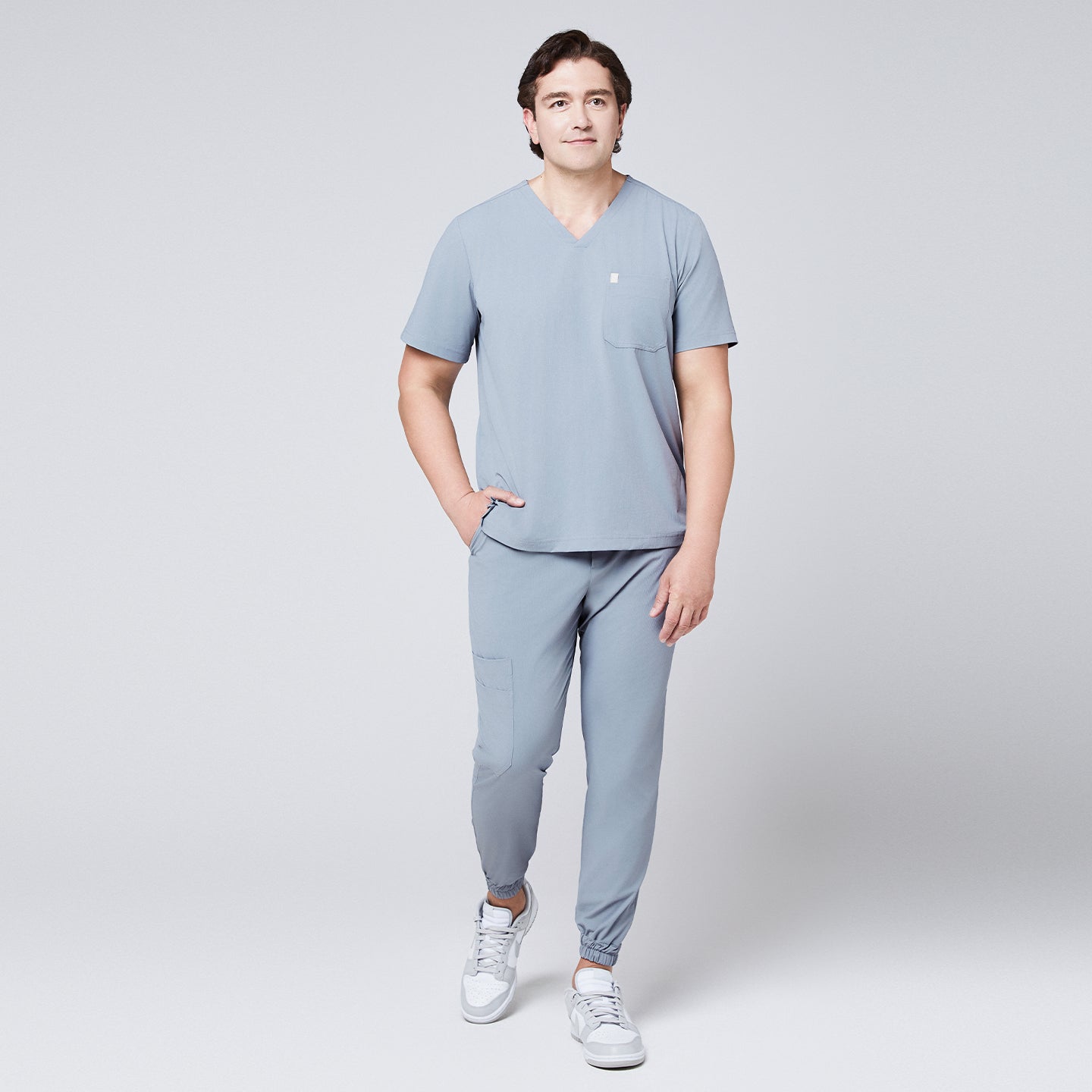 Model wearing cool gray jogger scrub pants with elastic cuffs and a matching V-neck scrub top, paired with gray Nike sneakers,Cool Gray