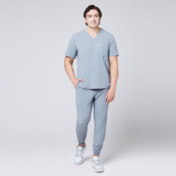 Image of Model wearing cool gray jogger scrub pants with elastic cuffs and a matching V-neck scrub top, paired with gray Nike sneakers,Cool Gray