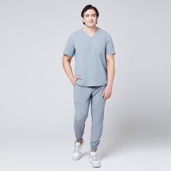 Image of A man wearing a Cool Gray Single Pocket Scrub Top and Cool Gray StretchFit Jogger Scrub Pants, shown in a full-length view while walking,Ash Gray