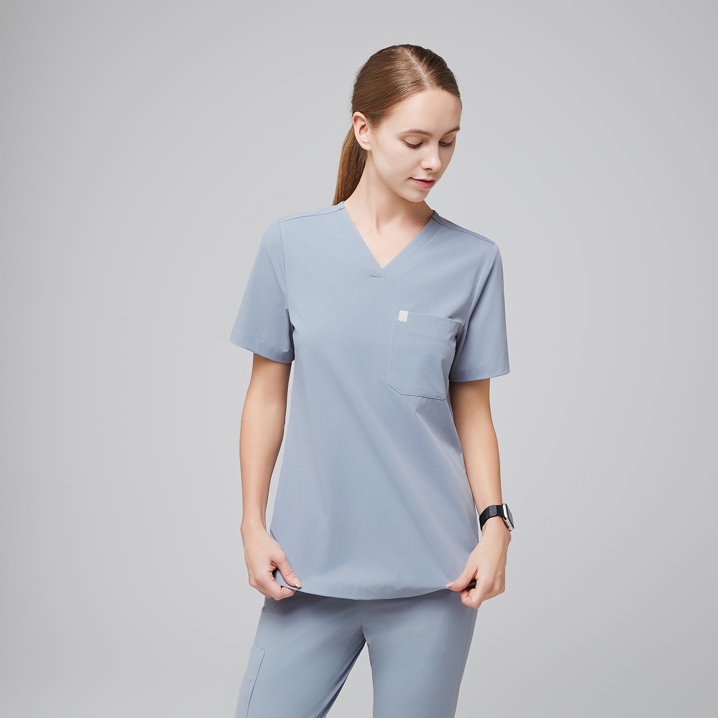 Female healthcare professional in a cool gray scrub top and pants, adjusting the hem of the top,Cool Gray