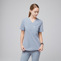 Image of Female healthcare professional in a cool gray scrub top and pants, adjusting the hem of the top,Cool Gray