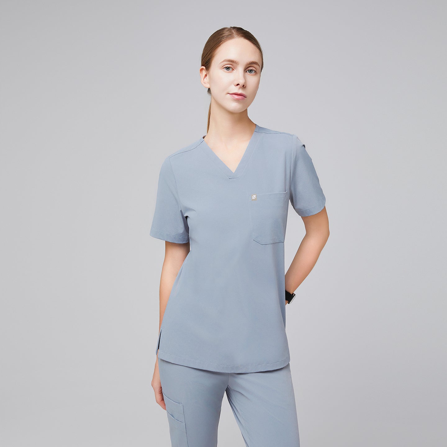 Female healthcare professional wearing a cool gray scrub set with a single pocket, standing in a relaxed pose,Cool Gray