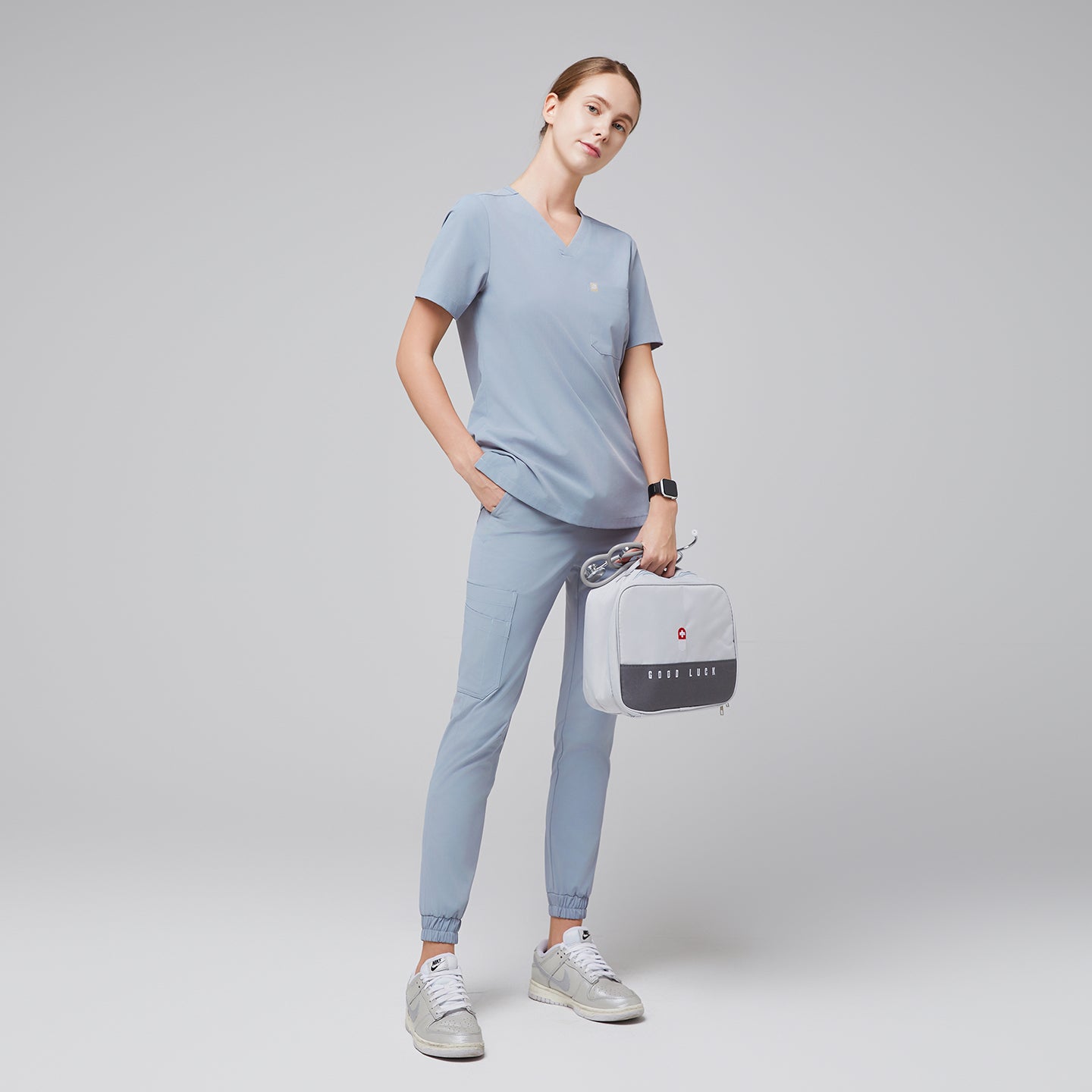 Female healthcare professional in a cool gray scrub set, holding a light gray medical kit bag and wearing silver sneakers, full-body side view,Cool Gray