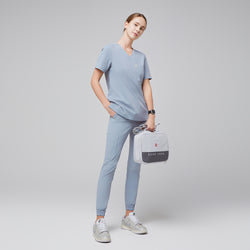 Image of Female healthcare professional in a cool gray scrub set, holding a light gray medical kit bag and wearing silver sneakers, full-body side view,Cool Gray