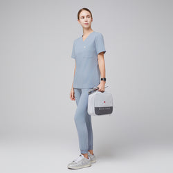 Image of Female healthcare professional in a cool gray scrub set, holding a light gray medical kit bag and wearing silver sneakers, standing in a relaxed pose,Cool Gray