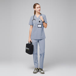 Image of Model wearing cool gray V-neck scrub top and straight-leg scrub pants, holding a medical kit and stethoscope,Cool Gray