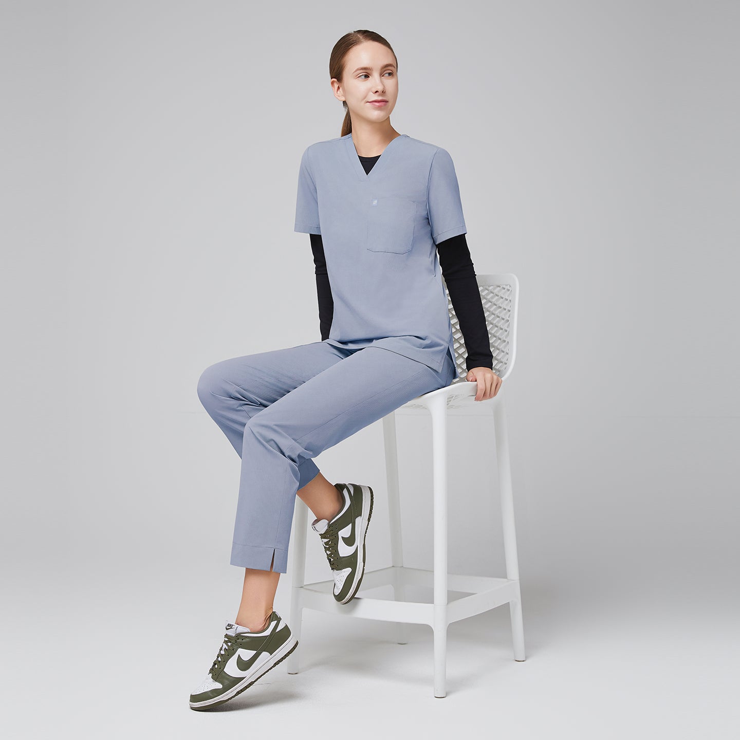 Model seated, wearing cool gray scrubs with black long-sleeve undershirt and green sneakers,Cool Gray