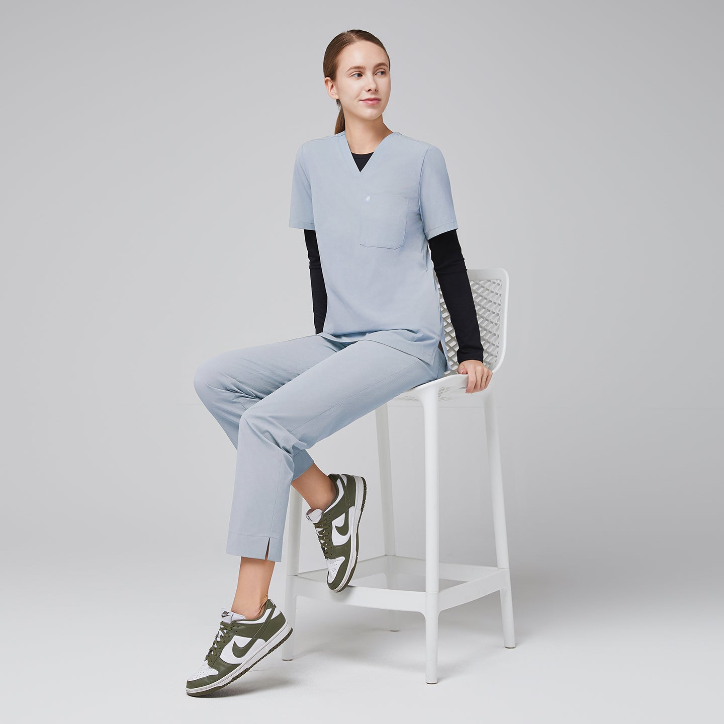 Model seated, wearing cool gray scrubs with black long-sleeve undershirt and green sneakers,Cool Gray