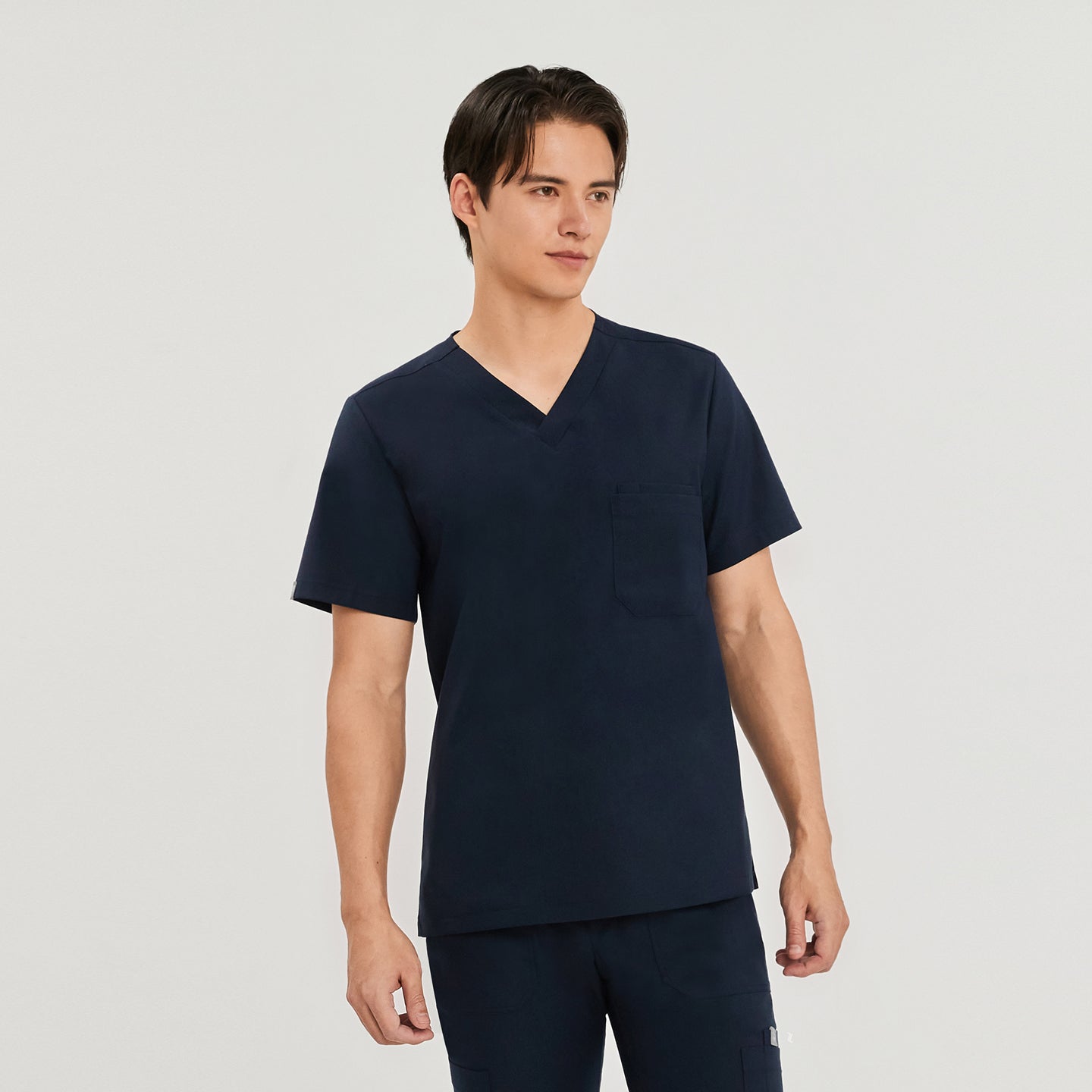 Male model wearing a navy scrub top with a V-neck and a single chest pocket, standing against a plain background,Navy