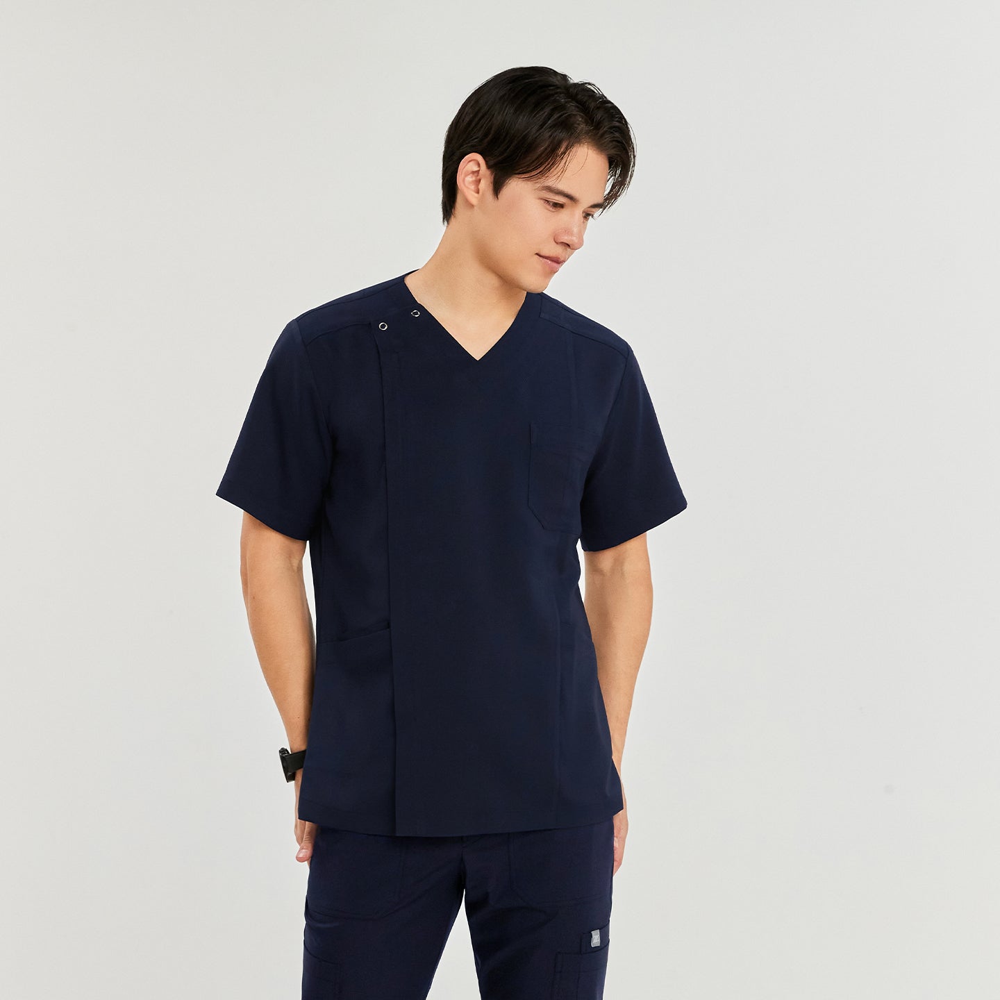 Man in a front zipper scrub top with chest and side pockets, matching straight-leg pants, looking to the side with hands in pockets,Navy