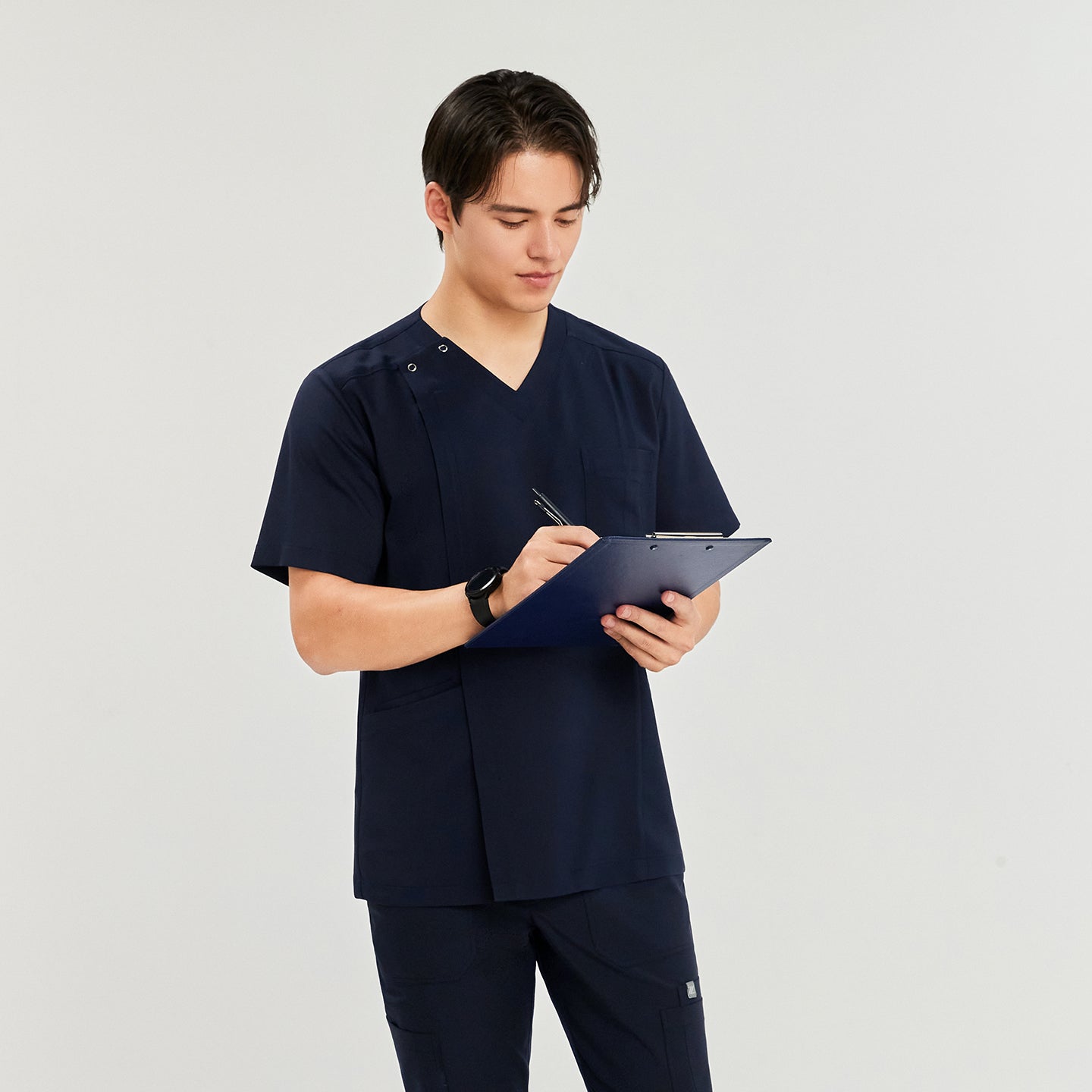 Man wearing a front zipper scrub top with chest and side pockets, matching cargo pants, holding a blue clipboard and pen,Navy