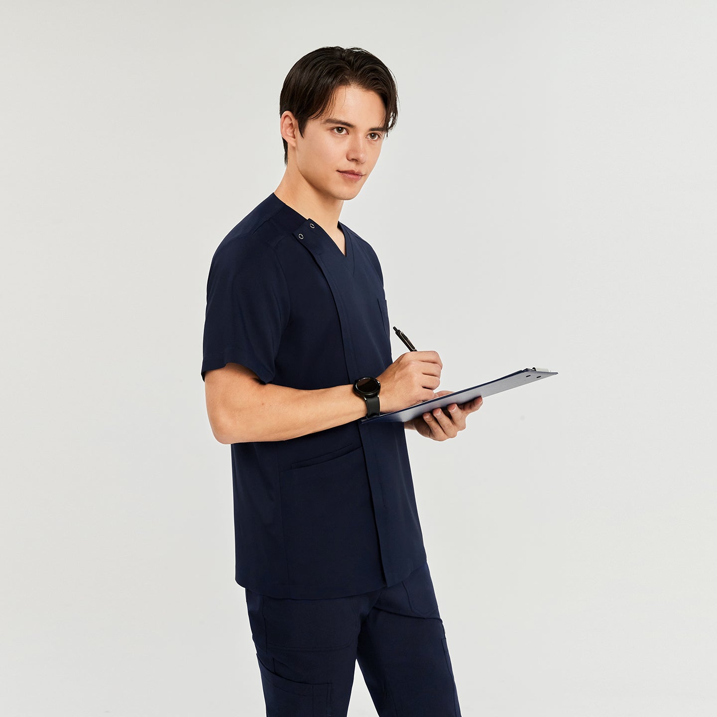 Man in a front zipper scrub top with chest and side pockets, matching straight-leg pants, holding a clipboard and pen,Navy