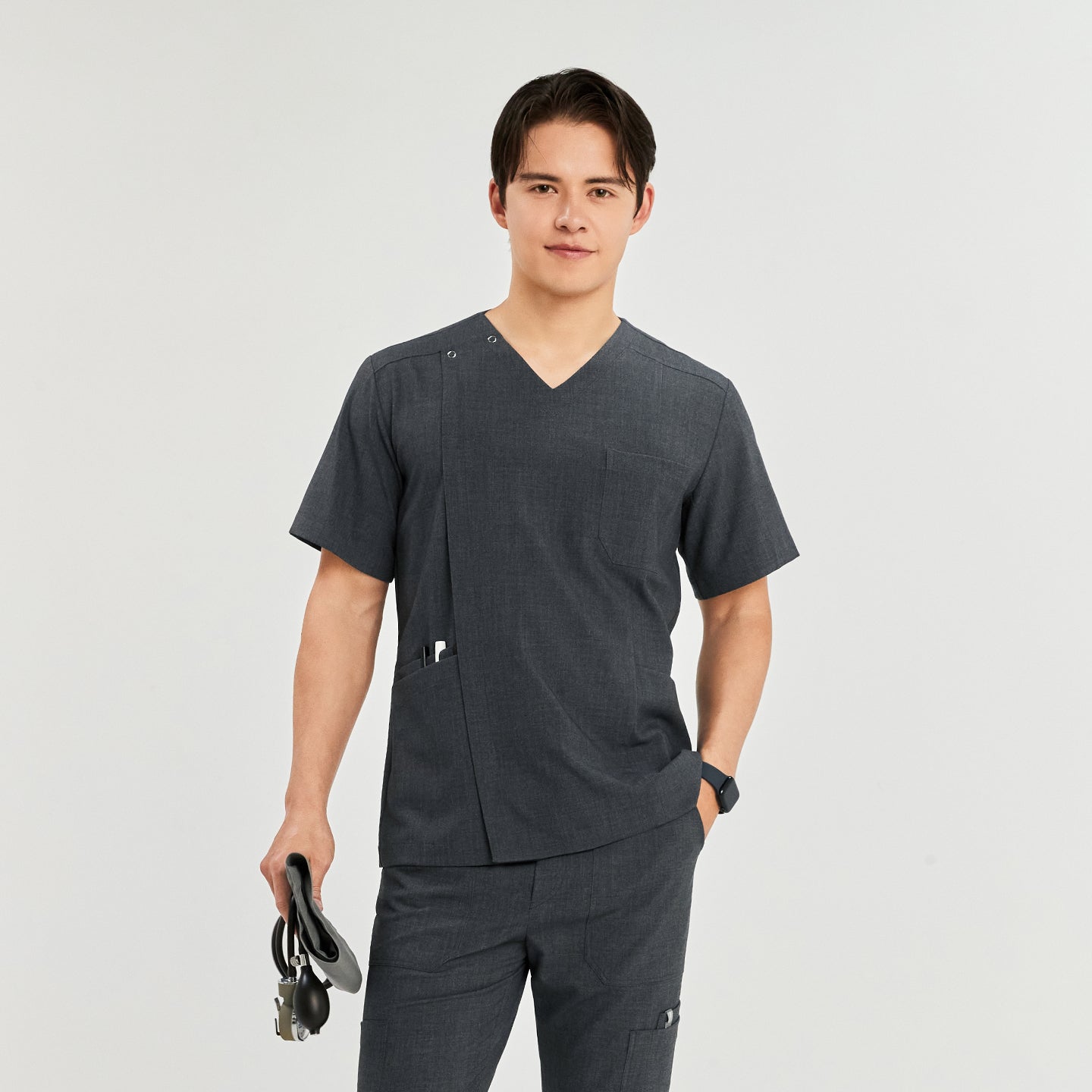 Man wearing a front zipper scrub top with matching cargo pants, holding a blood pressure monitor, one hand in pocket,Charcoal Gray