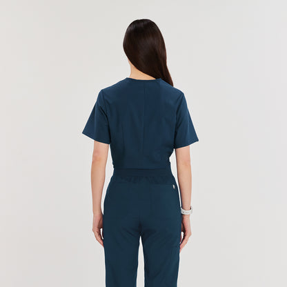 Woman wearing a dark blue soft stretch scrub top and matching pants, standing with her back to the camera. Long hair is draped over her back,Dark Blue