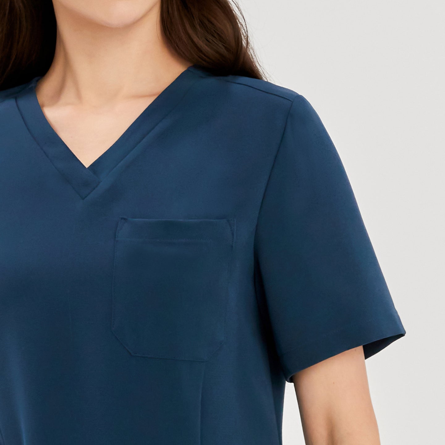 Close-up of a woman wearing a dark blue soft stretch scrub top, showing the V-neck and chest pocket details,Dark Blue