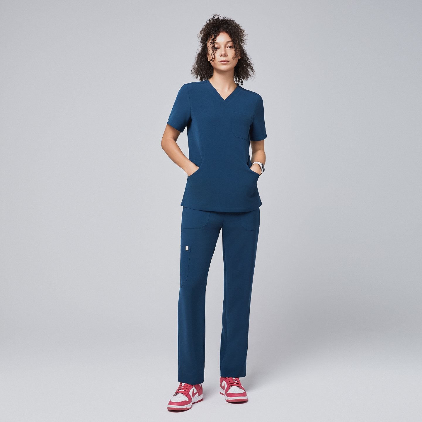 Model wearing the dark blue scrub top and pantst, featuring a V-neck, short sleeves, and functional pockets, paired with pink sneakers,Dark Blue