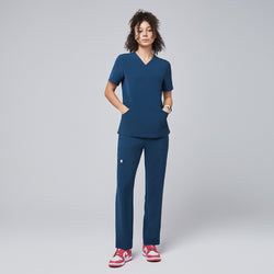 Image of Model wearing the dark blue scrub top and pantst, featuring a V-neck, short sleeves, and functional pockets, paired with pink sneakers,Dark Blue