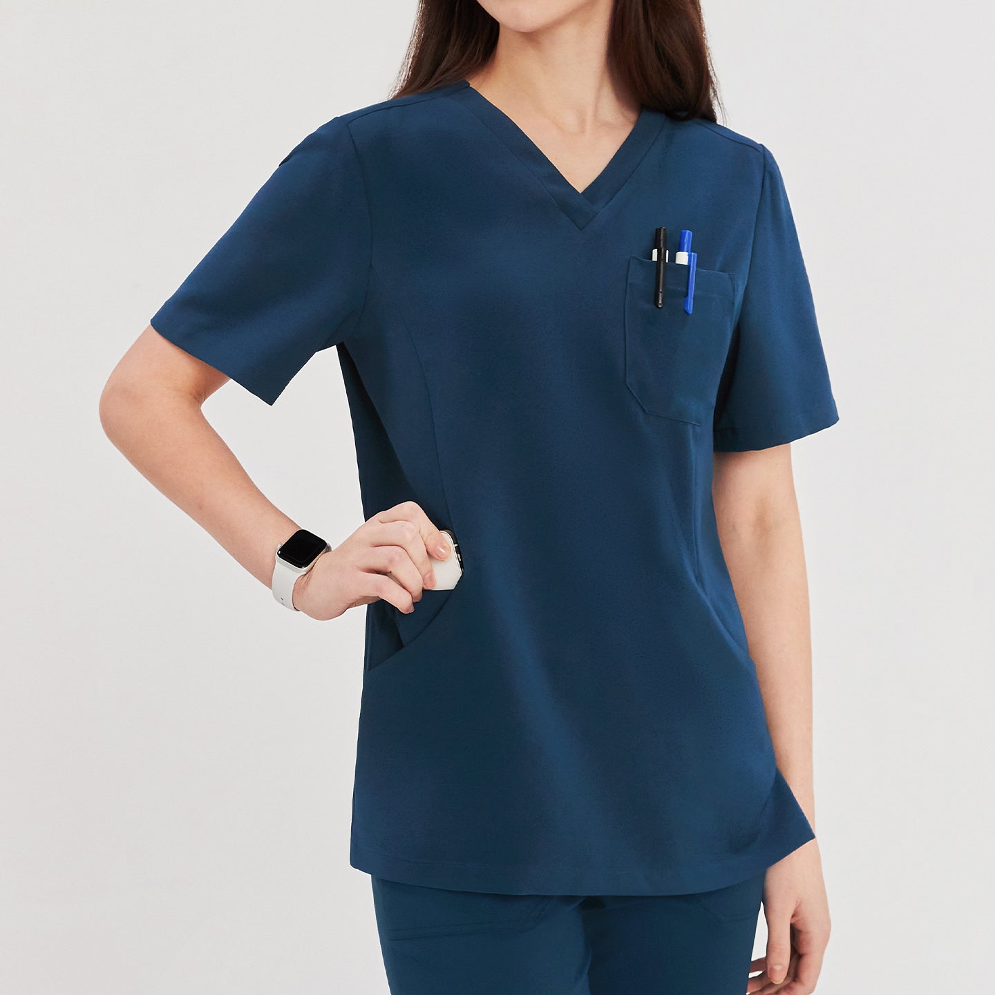 Close-up of a woman wearing a dark blue soft stretch scrub top, showing the chest pocket with pens and side pocket details, with a smartwatch on her wrist,Dark Blue