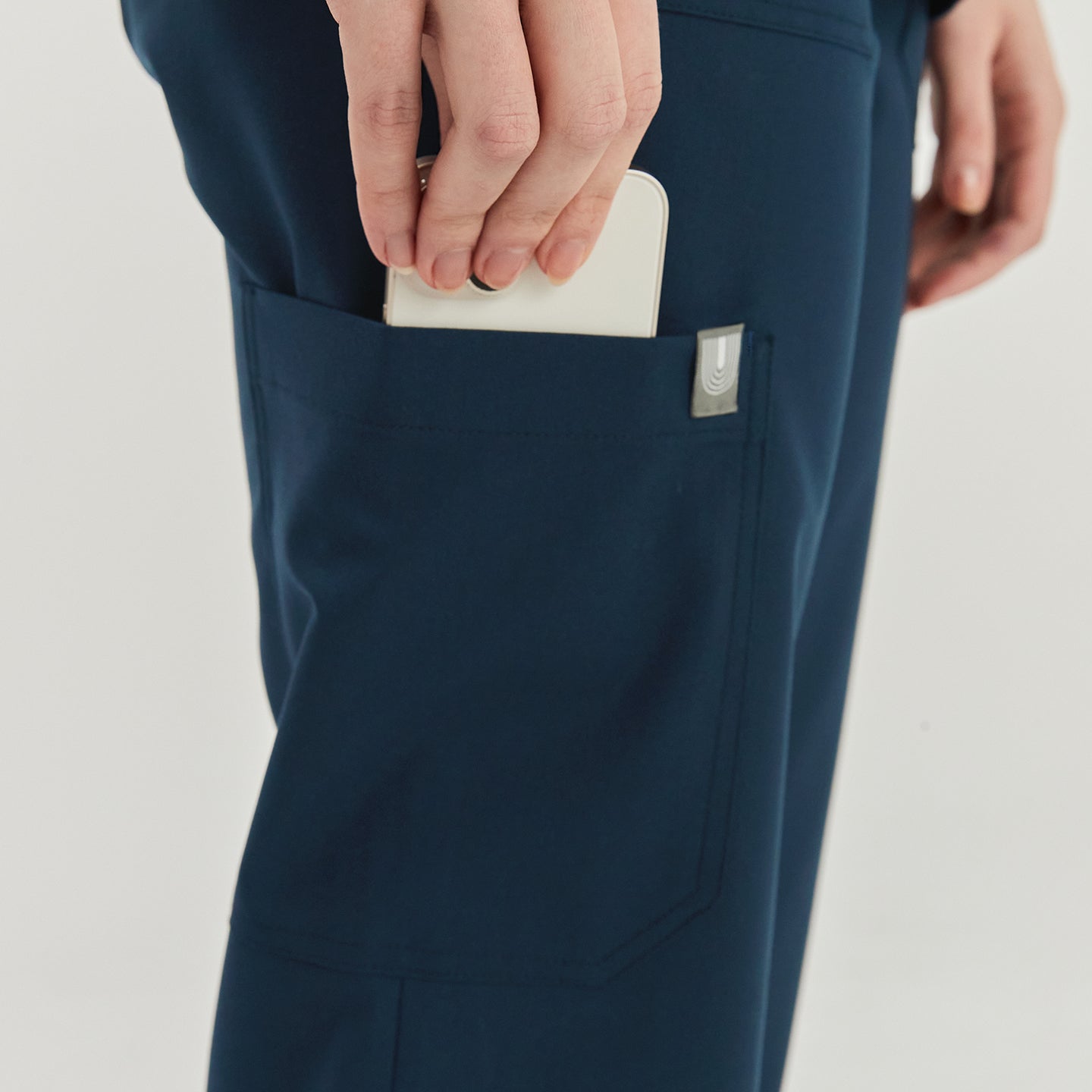 Close-up of a woman placing a smartphone into the side pocket of dark blue split hem scrub pants, showcasing the practical pocket detail,Dark Blue