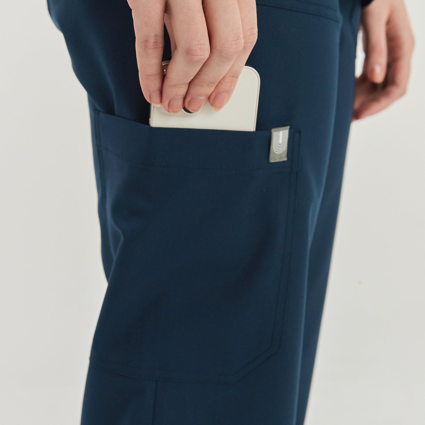 Close-up of a woman placing a smartphone into the side pocket of dark blue zipper slit scrub pants, showcasing the practical pocket detail,Dark Blue
