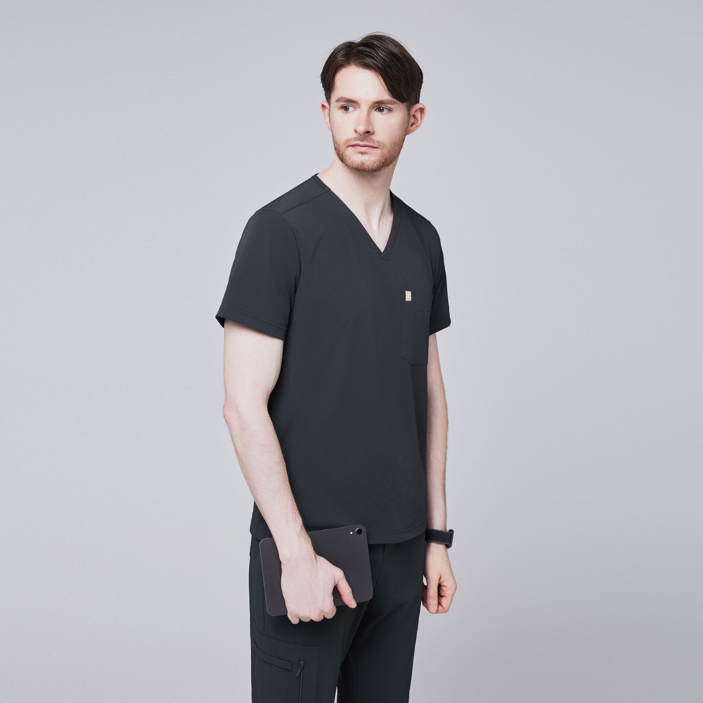 Male model wearing a deep gray V-neck single-pocket scrub top, holding a tablet,Deep Gray