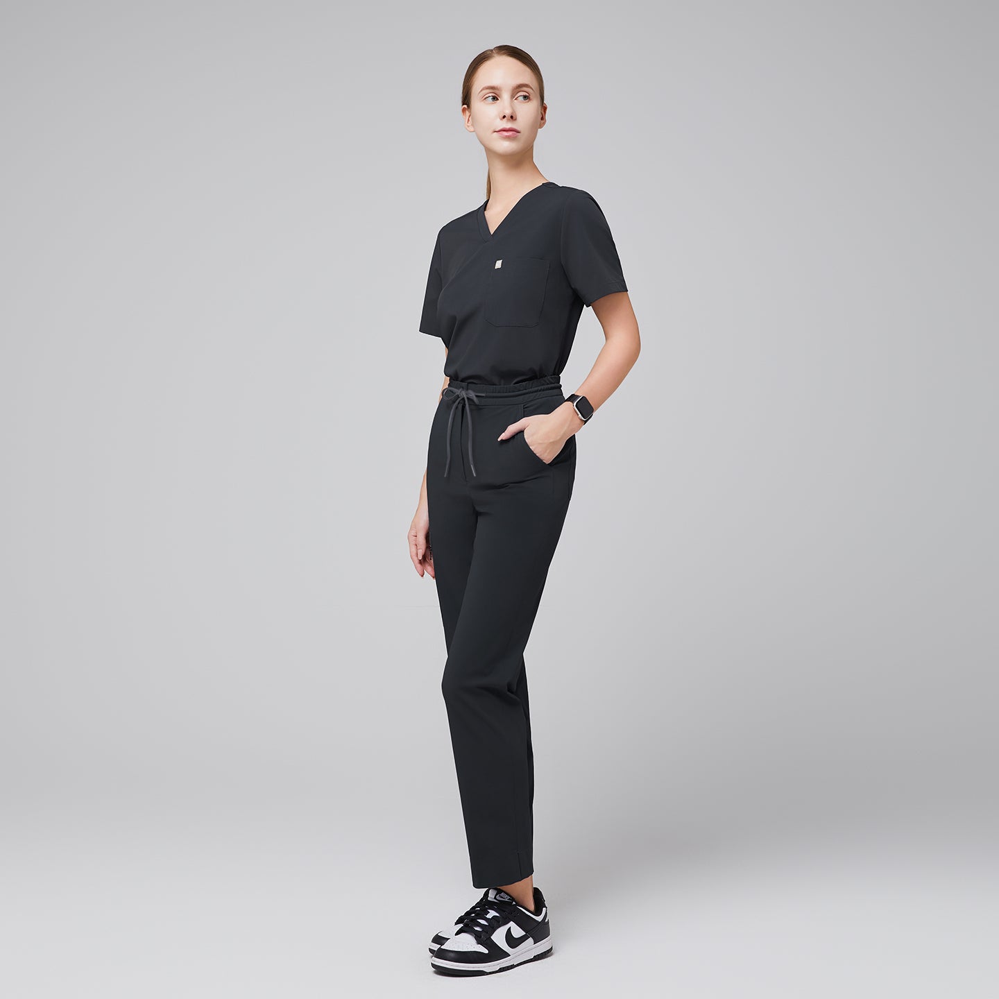 Full-body view of deep gray scrub set featuring a single-pocket V-neck top and drawstring pants, paired with black and white sneakers,Deep Gray