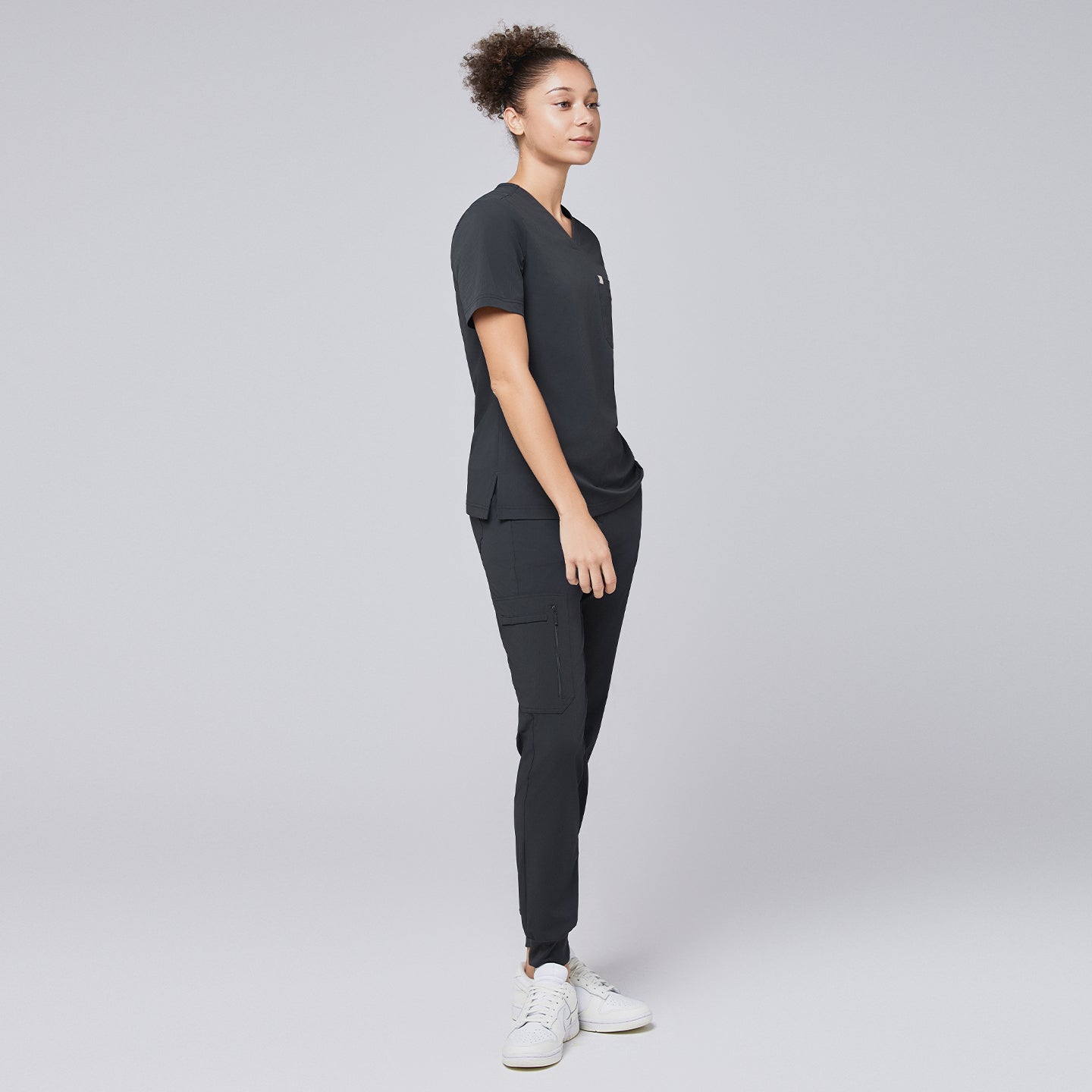 Side view of a model wearing deep gray jogger scrub pants with zipper pocket and matching scrub top, paired with white sneakers,Deep Gray