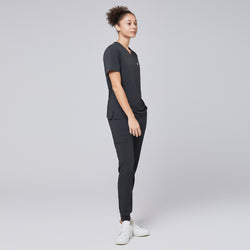 Image of Side view of a model wearing deep gray jogger scrub pants with zipper pocket and matching scrub top, paired with white sneakers,Deep Gray