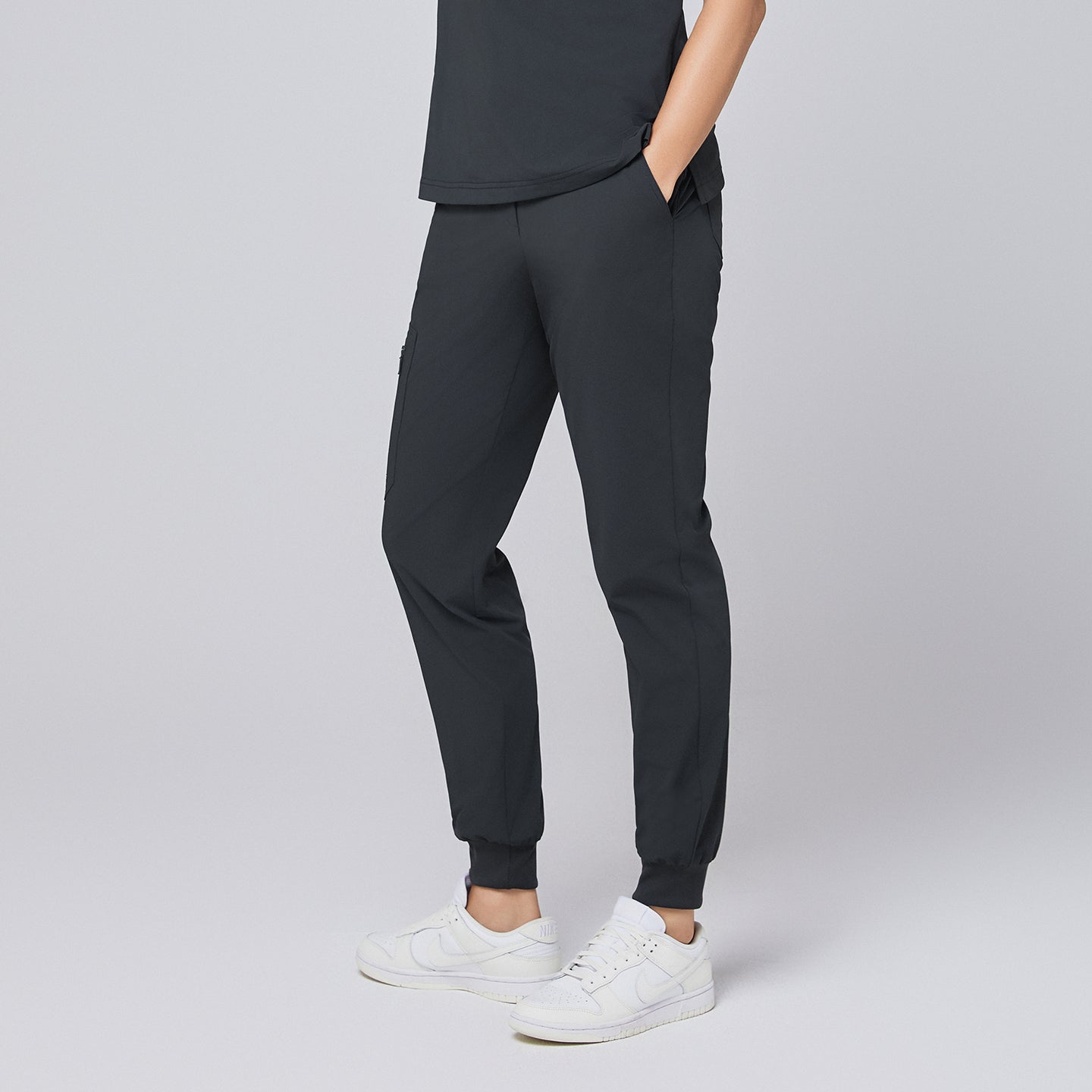 Side angle of deep gray jogger scrub pants with zipper pocket and elastic cuffs, styled with white sneakers,Deep Gray