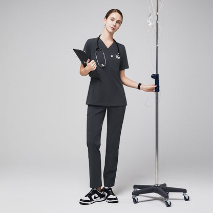 Female healthcare professional in gray scrubs with zipper pocket pants, holding a clipboard and standing next to an IV stand,Deep Gray