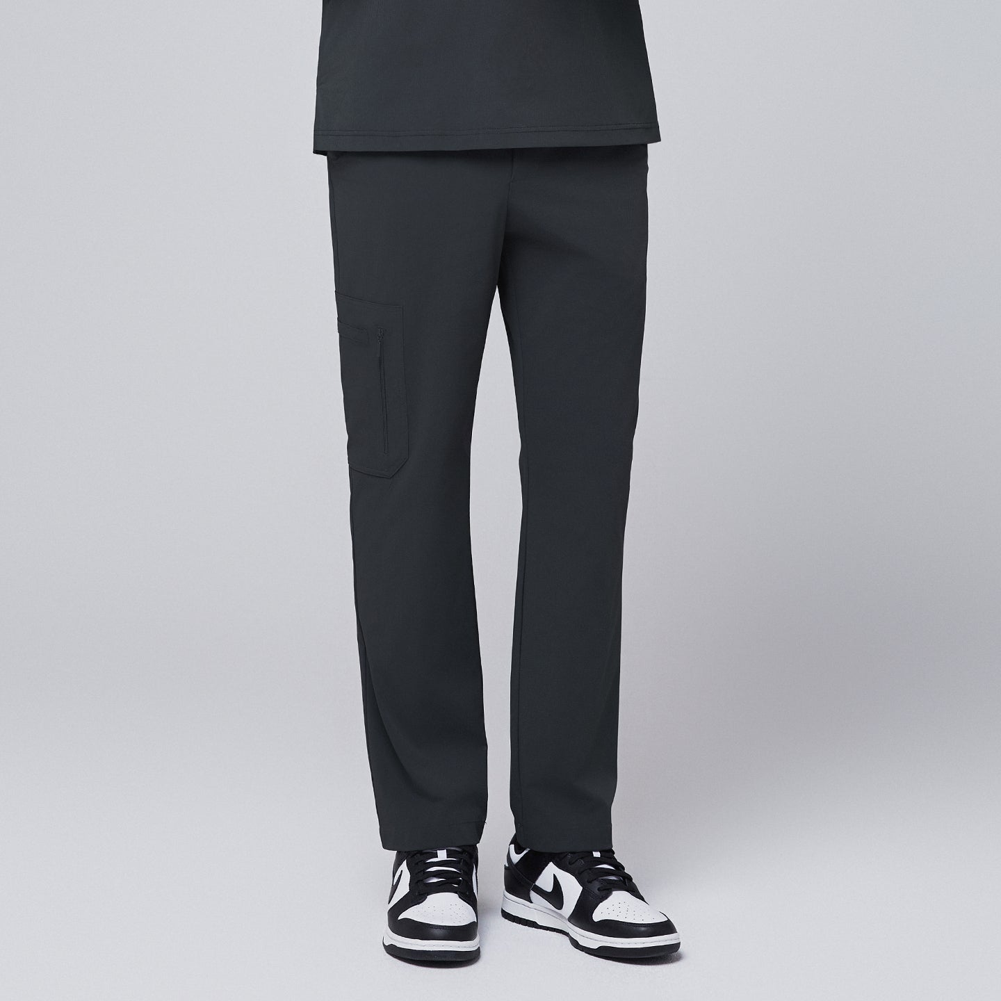 Front view of deep gray scrub pants featuring a sleek zipper pocket on the side, paired with black and white sneakers, modeled against a neutral gray background,Deep Gray